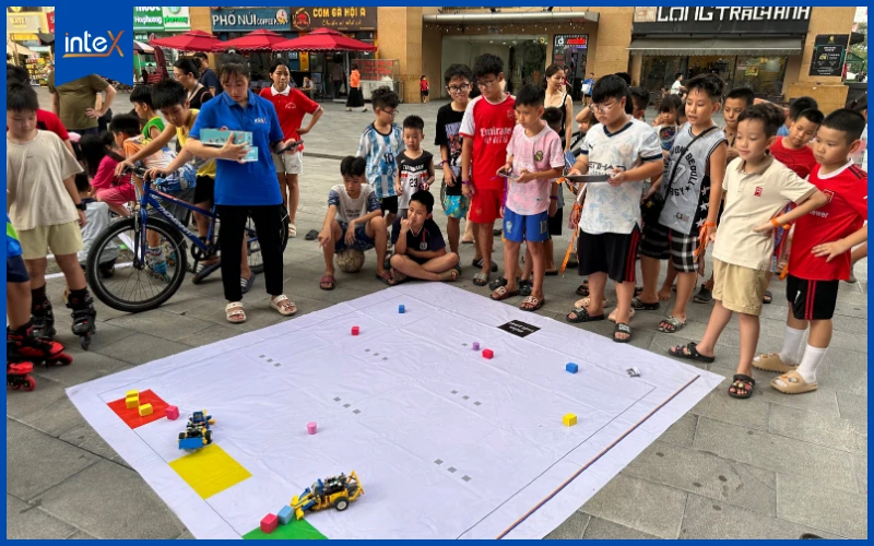 Trẻ em tham gia cuộc thi lập trình và điều khiển robot trên sân đấu ngoài trời, thu hút đông đảo khán giả.